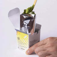 Spoonful of Tsukikage autumn release matcha green tea from foil packaging in box on bamboo tea ladle against white background