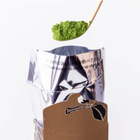Heaping scoop of green matcha powder on chashaku bamboo tea ladle above opened foil pouch from autumn Tsukikage matcha