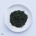 White plate of dark green dried crisp loose leaf Japanese Unro Sencha tea leaves by Ippodo Tea Co. on white table