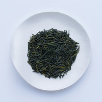 White plate of dark green dried crisp loose leaf Japanese Unro Sencha tea leaves by Ippodo Tea Co. on white table