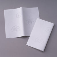 Folded set of white Kaishi Tissues resting on one unfolded Kaishi tissue with subtle fruit and plant designs on grey table