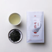 Teacup of brewed straw-colored gyokuro green tea alongside plate of dark green tea leaves and packaging for Kanro Ippodo Tea