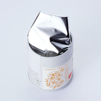 Decorative metal tin can of Ippodo Tea Sayaka matcha powder with floral tea pot logo open lid and foil on white background