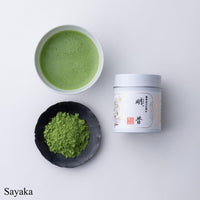 Teacup of bright green usucha matcha tea beside black plate of loose tea powder and white tin of Sayaka Matcha by Ippodo Tea 