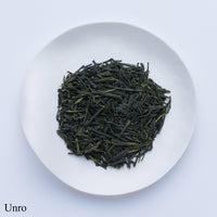 White plate of dark green dried crisp loose leaf Japanese Unro Sencha tea leaves by Ippodo Tea Co. on white table