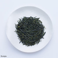 Ippodo Tea Kumpu sencha sample depicting loose green needle-like rolled futsumushi tea leaves on white plate on white table 
