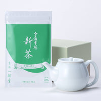 White porcelain Hakuji teapot in front of bright green and white pouch of Uji Shincha tea with Japanese writing and beige box