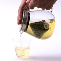 Green tea poured from Ippodo Tea branded glass teapot with stainless steel strainer lid and one-pot teabag inside into glass