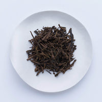 Sample of Ippodo Hojicha roasted green tea leaves and stems on white plate, on white table