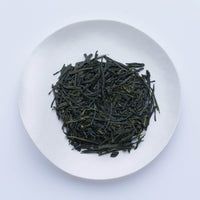 White plate of dark green dried loose leaf Japanese Hosen Sencha most popular tea leaves by Ippodo Tea Co. on white table