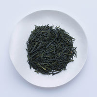 White plate of dark green premium high-grade loose leaf Ippodo Tea Kaboku Sencha Japanese tea leaves on white table