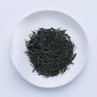 White plate of dark green premium high-grade loose leaf Ippodo Tea Kumpu Sencha Japanese tea leaves on white table