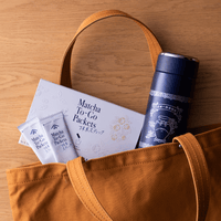 Box of Matcha-To-Go with two individual packets and tall navy tin of Ippodo Tea peeking out of top of brown canvas tote bag