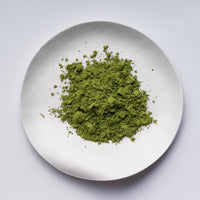 Green loose Japanese Ippodo Tea Organic Matcha tea powder on silver plate on white table