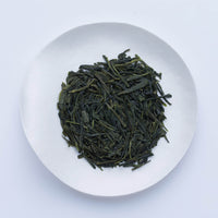 White plate of medium dark green loose leaf Ippodo Tea Organic Sencha tea leaves on white table