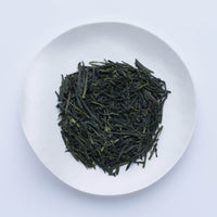 White plate of dark green classic loose leaf Ippodo Tea Shoike Sencha Japanese tea leaves on white table