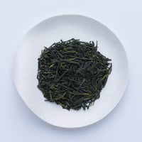 White plate of dark green dried crisp loose leaf Japanese Unro Sencha tea leaves by Ippodo Tea Co. on white table