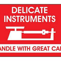 Red fragile sticker that says "delicate instruments - handle with great care" in white with picture of delicate machine