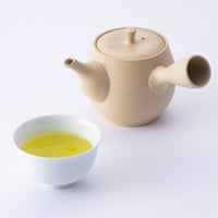White teacup of yellow brewed Ippodo Genmaicha bancha green tea with roasted rice beside Japanese artisan-made teapot kyusu