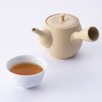 White teacup of brewed Ippodo Hojicha bancha green tea beside Japanese artisan-made artistic teapot kyusu on white table