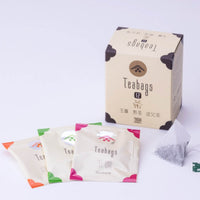 Teabag Assortment box beside various sealed Ippodo Japanese teabag packets and one open pyramid teabag on white table