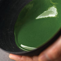 Vivid green smooth thick koicha Ippodo premium Kanza Matcha sticking to sides of tilted black artisan-made ceramic tea bowl