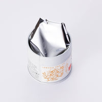 Decorative metal tin can of Ippodo Tea Horai matcha powder with floral tea pot logo open lid and foil on white background