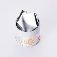 Decorative metal tin can of Ippodo Tea Shoin matcha powder with floral tea pot logo open lid and foil on white background