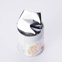 Decorative metal tin can of Ippodo Tea Ummon matcha powder with floral tea pot logo open lid and foil on white background