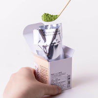 Scooping matcha powder with bamboo tea ladel from foil package inside box of Ikuyo matcha with instructions on back showing