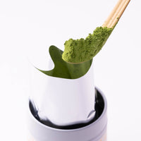 Heaping scoop of green matcha powder on chashaku bamboo tea ladle above opened foil pouch of Organic Matcha tin
