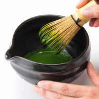 Holding black tea bowl with spout whisking thick koicha Ippodo Tea Shoin matcha with Chasen bamboo 80-tip whisk white table