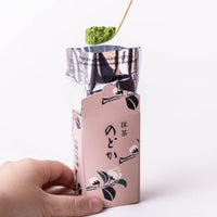 Holding pale pink decorative box of Nodoka matcha with opened foil and scooping bright green matcha tea powder with ladle