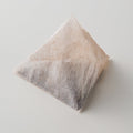 Single pyramid-shaped large one-pot teabag filled with Ippodo Tea Co. mugicha coarsely cracked barley set atop white table