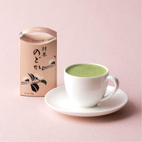 Pale pink Japanese floral box of Nodoka matcha next to white teacup filled with green matcha tea on saucer on pink background