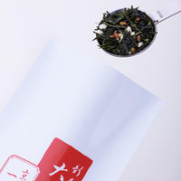 Stainless steel tablespoon measure of genmaicha green tea mixed with roasted rice scooped from red and white bag of Obukucha