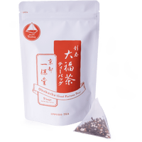 Pyramid shaped teabag of genmaicha green tea and roasted rice beside package of Obukucha Good Fortune Tea Teapot-Size Teabags