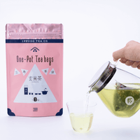 Pouring green tea from glass teapot holding a large one-pot teabag into Ippodo-branded glass beside pink package of Genmaicha