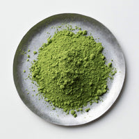 Green loose Japanese Premium Organic Matcha tea powder by Ippodo Tea on silver plate on white table