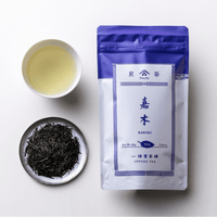 Teacup of brewed light green sencha tea alongside plate of dark tea leaves and purple packaging for Ippodo Kaboku Sencha
