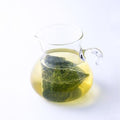 Small glass pitcher containing steeped golden futsumushi New Harvest Sencha green tea and submerged large one-pot teabag