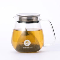 White pyramid shaped One-Pot Teabag of Ippodo Iribancha steeping in smoky brown tea in glass kyusu teapot