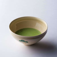 Green thin usucha straight matcha with light green frothy bubbles on surface in cream colored ceramic tea bowl with design