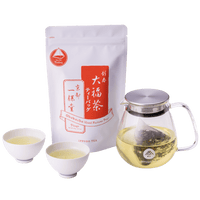 Two small white teacups of light green tea with a glass teapot of a teapot-size teabag in brewed tea and package of Obukucha