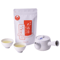 Large white porcelain teapot with two small white teacups with light green tea beside package of Obukucha Teapot-Size Teabags