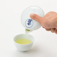 Pouring green tea from white porcelain Kiyomizu-yaki kyusu teapot with blue Japanese characters into white porcelain teacup