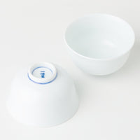 Two white porcelain Japanese teacups, one flipped upside down revealing Ippodo Tea seal on bottom, on white table