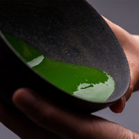 Vivid green smooth thick koicha Ippodo Premium Select Matcha sticking to sides of tilted black artisan-made ceramic tea bowl