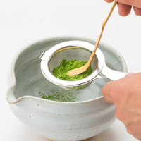 Green Ippodo matcha tea powder sifted through Chakoshi tea strainer into spouted tea bowl with Chashaku bamboo tea ladel