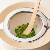 Vibrant green Ippodo matcha powder being sifted through Chakoshi tea strainer into tea bowl using Chashaku bamboo tea ladel